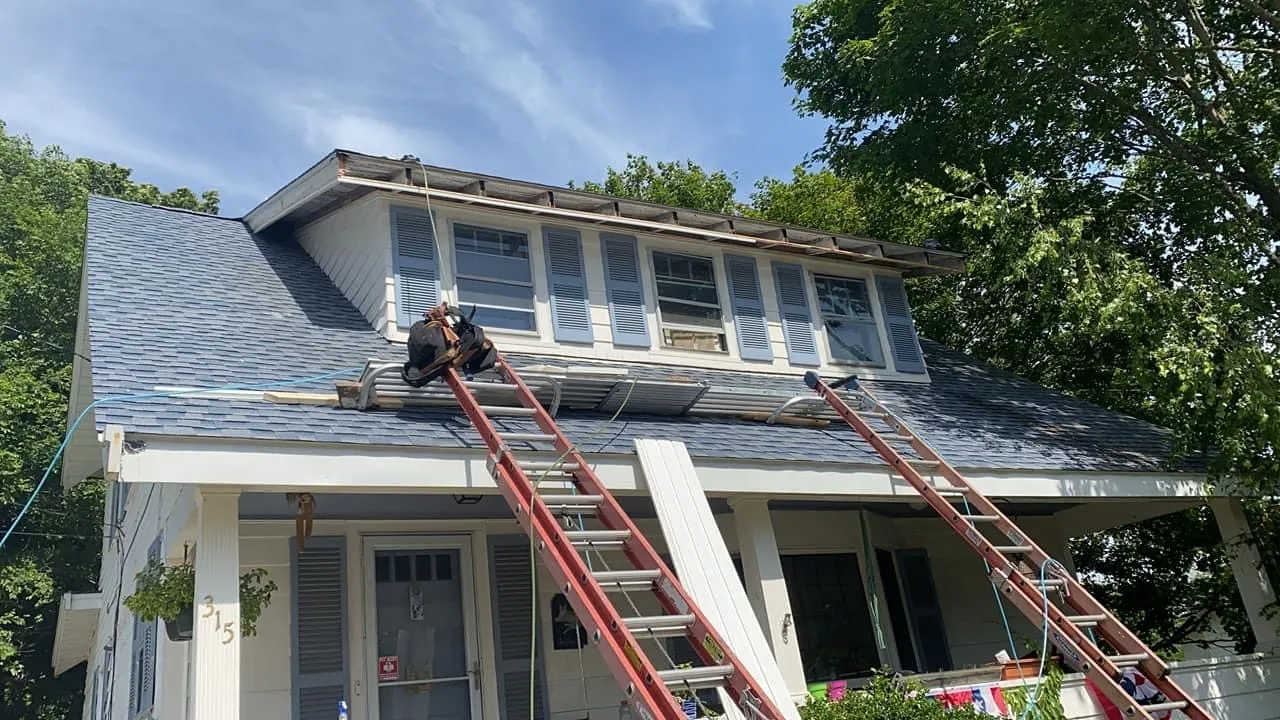 Two-story white home during gutter installation with ladders set at the roofline