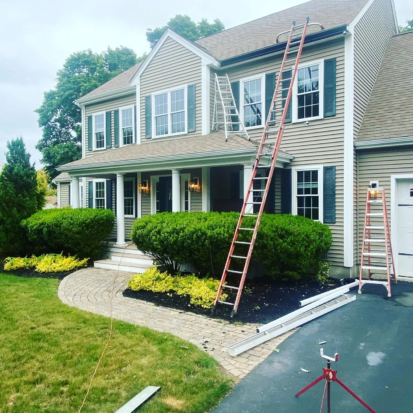 Colonial home with ladders set up at the roofline during seamless gutter work