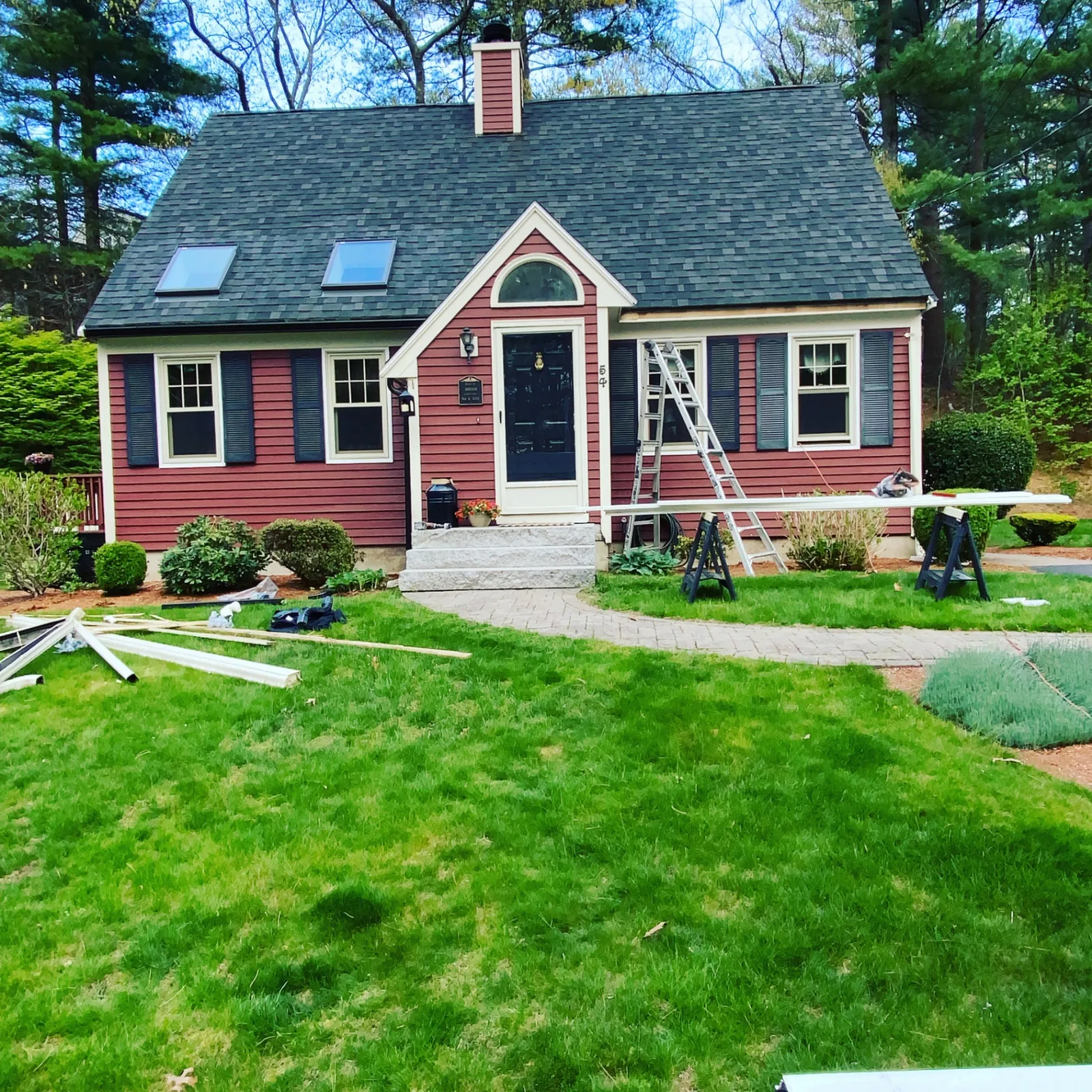 Red cape-style home with gutter materials and ladders set up during installation